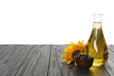 Photo of Sunflower, bottle of oil and seeds on black wooden table against white background, space for text