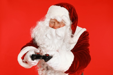 Photo of Authentic Santa Claus with game controller on red background