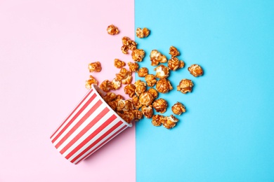 Photo of Overturned paper cup with caramel popcorn on color background, top view