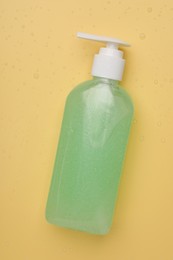 Photo of Wet bottle of face cleansing product on pale orange background, top view