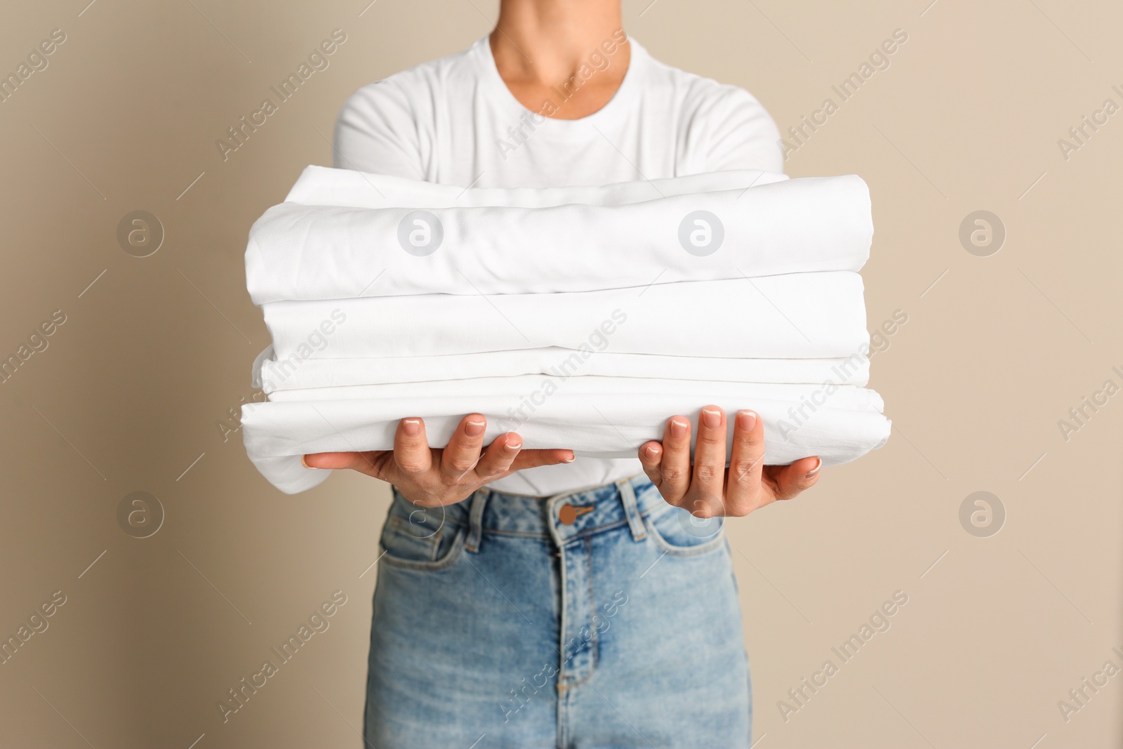 Photo of Woman holding stack of clean bed linens on beige background