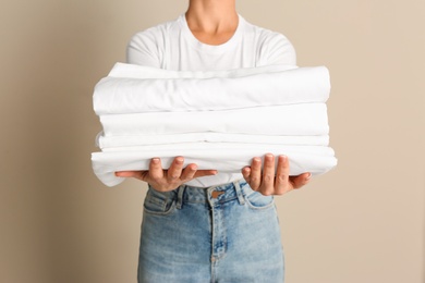 Woman holding stack of clean bed linens on beige background