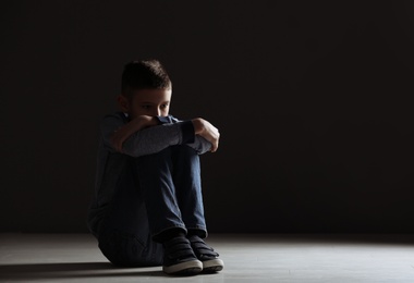 Photo of Upset boy sitting in dark room. Space for text