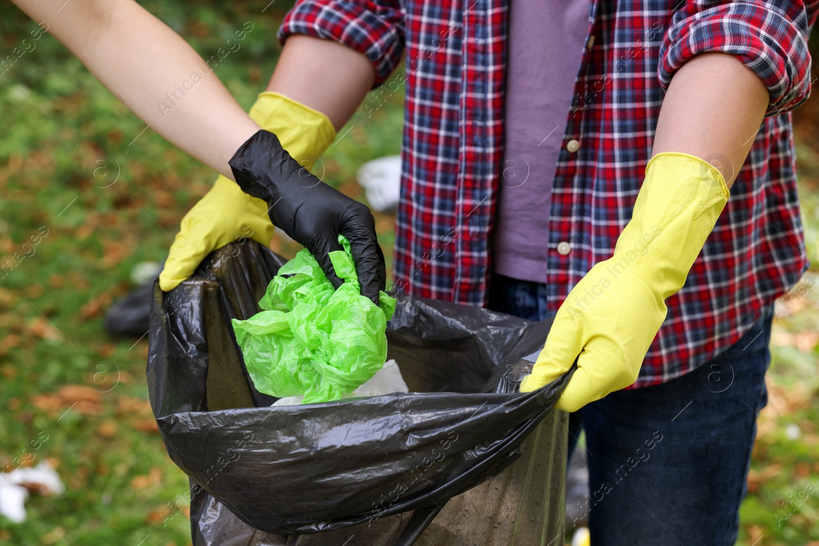 Photo of Man and woman with plastic bag collecting garbage in park, closeup