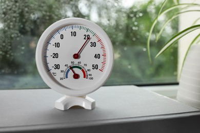 Photo of Round mechanical hygrometer on book near window. Space for text