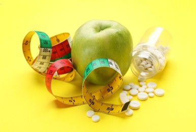 Photo of Weight loss pills, apple and measuring tape on yellow background