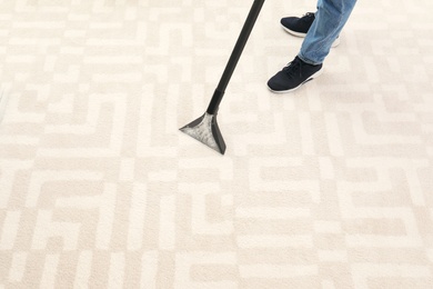 Man removing dirt from carpet with vacuum cleaner indoors, closeup. Space for text