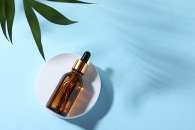 Photo of Bottle of cosmetic oil and leaves on light blue background, top view. Space for text