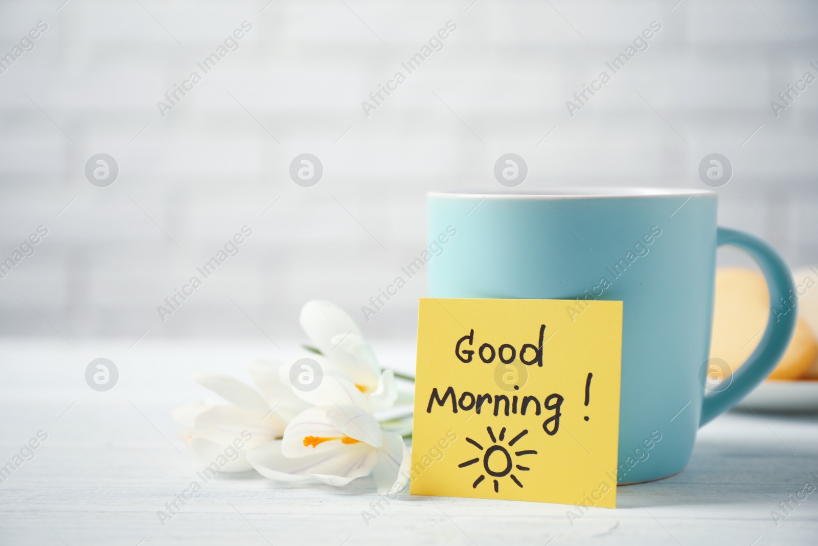 Photo of Delicious coffee, flowers and card with GOOD MORNING wish on white wooden table, closeup. Space for text