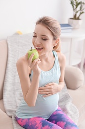 Photo of Young pregnant woman eating apple at home