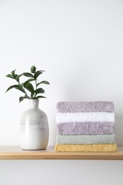 Photo of Stacked terry towels and green branches in vase on wooden shelf near white wall