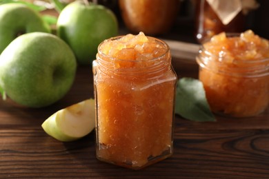 Glass jar of delicious apple jam and fresh fruits on wooden table, closeup