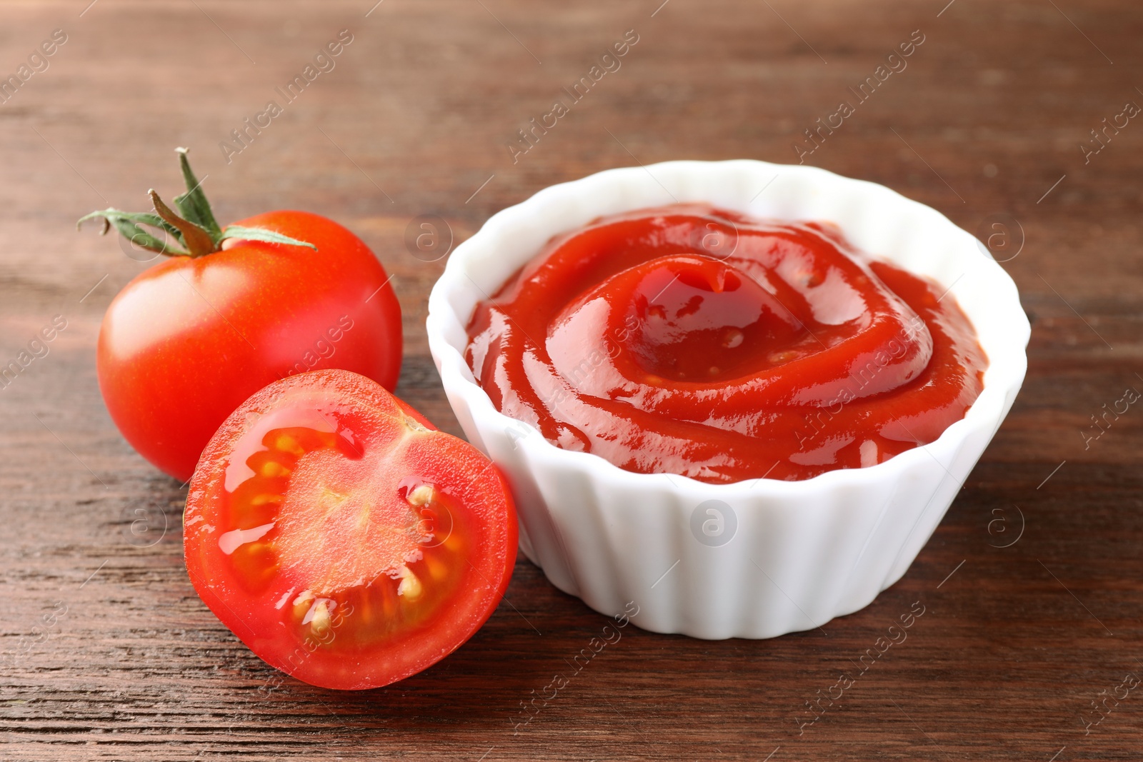 Photo of Bowl of tasty ketchup and tomatoes on wooden table, closeup