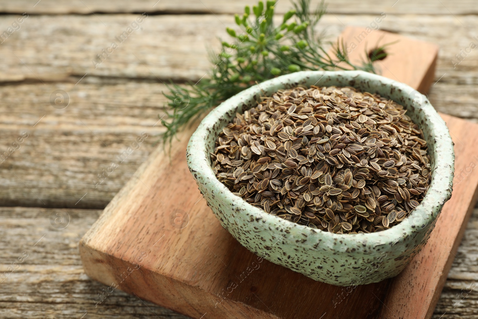 Photo of Board with bowl of dry seeds and fresh dill on wooden table, closeup. Space for text