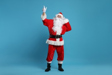 Photo of Merry Christmas. Santa Claus in headphones listening to music and pointing at something on light blue background