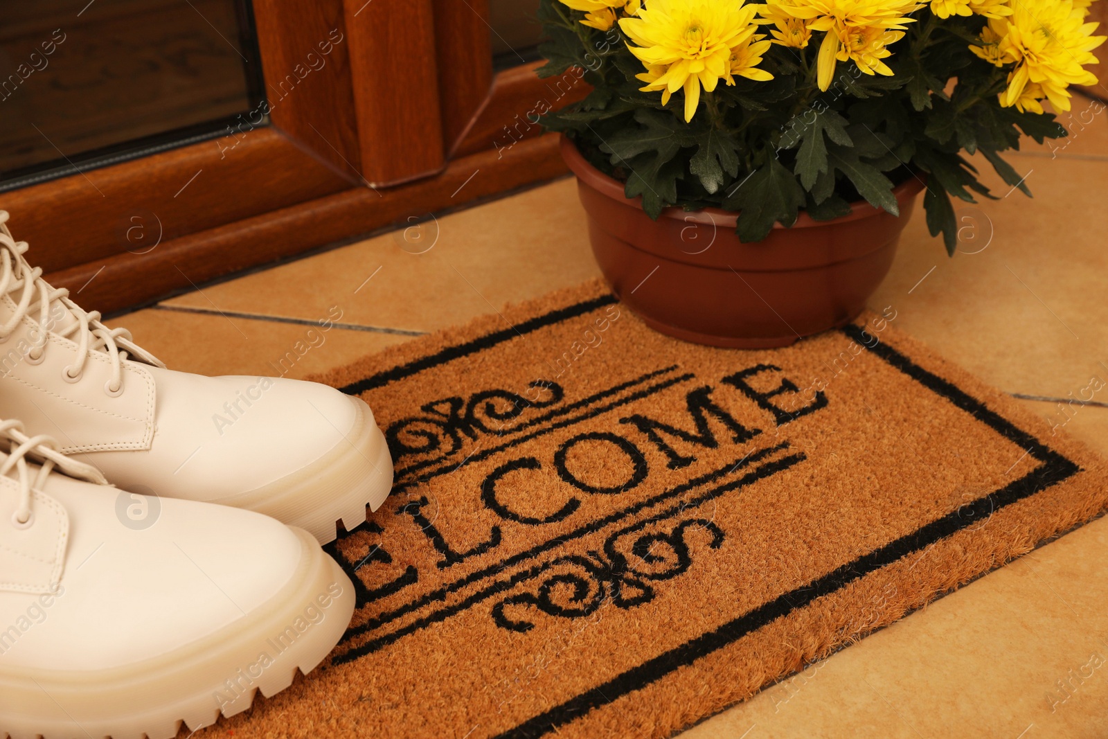 Photo of Door mat with word Welcome, stylish boots and beautiful flowers on floor