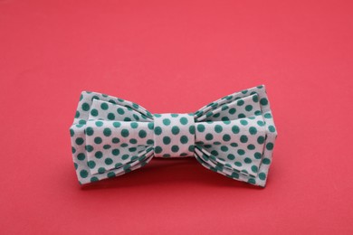 Photo of Stylish white bow tie with green polka dot pattern on red background