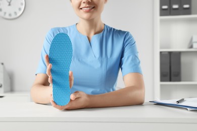 Photo of Female orthopedist showing insole at table in hospital, closeup