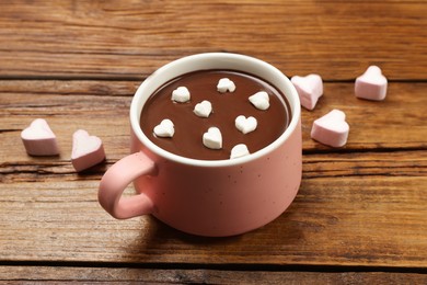 Photo of Cup of hot chocolate with heart shaped marshmallows on wooden table.