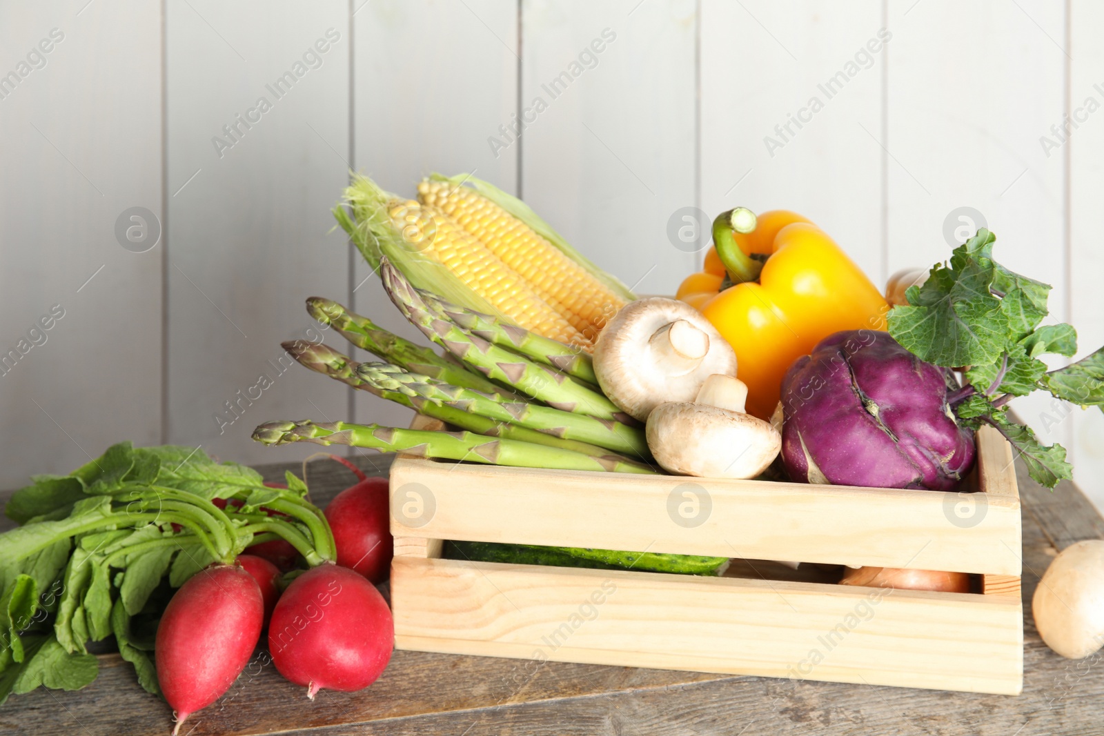 Photo of Crate with assortment of fresh vegetables on table against light background