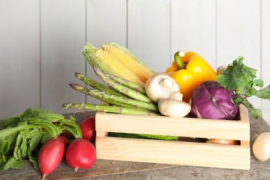 Photo of Crate with assortment of fresh vegetables on table against light background