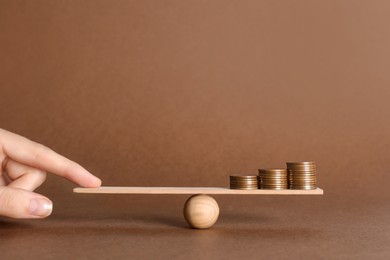 Photo of Woman balancing miniature seesaw with stacks of coins on brown background, closeup. Harmony concept