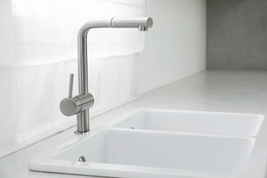 Photo of Modern sink and water tap near window in kitchen. Interior design