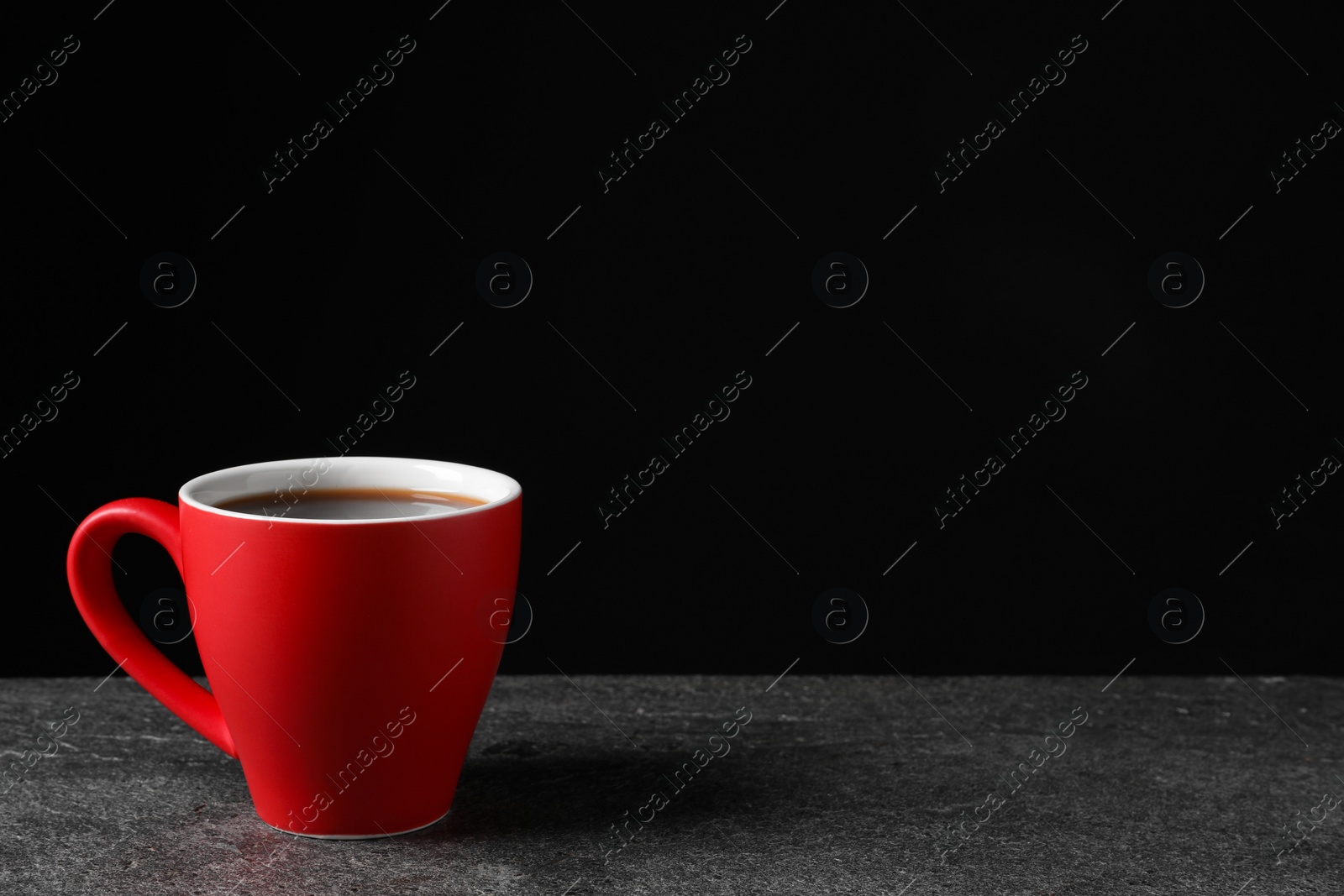 Photo of Red cup with aromatic coffee on grey textured table against black background. Space for text