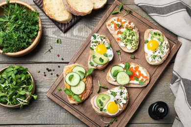 Different delicious sandwiches with microgreens on wooden table, flat lay