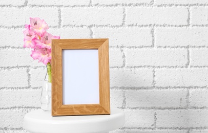 Blank frame and vase with flowers on table near brick wall. Mock up for design