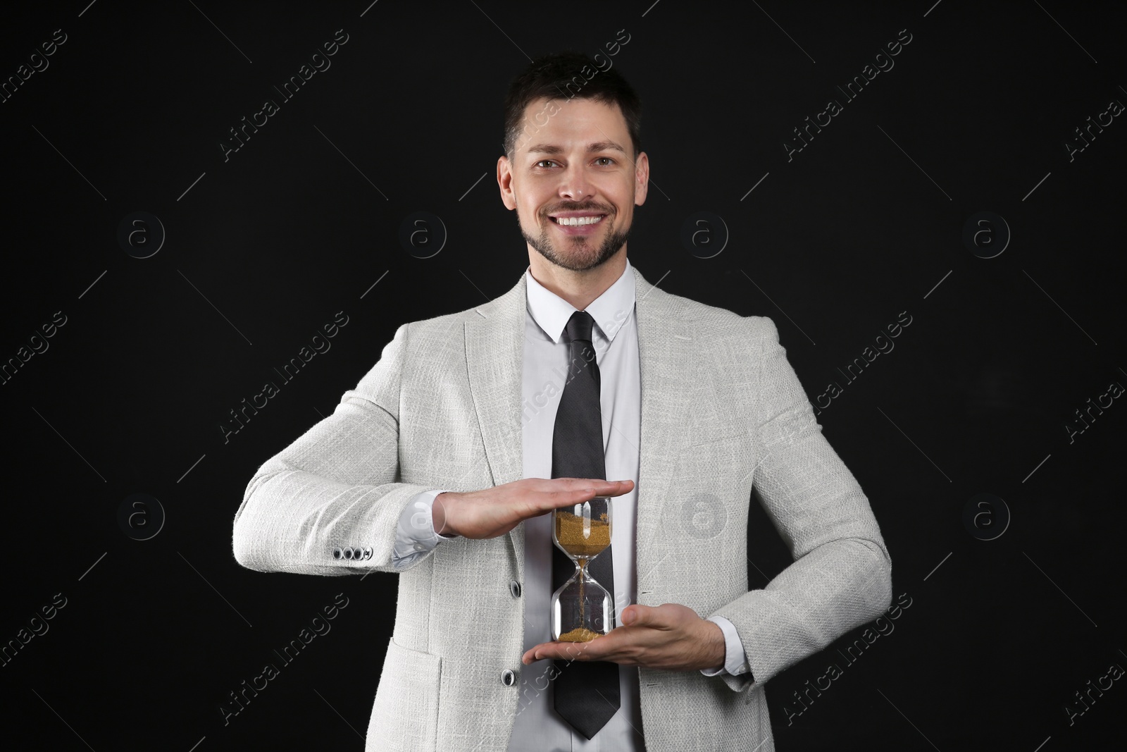 Photo of Happy businessman holding hourglass on black background. Time management