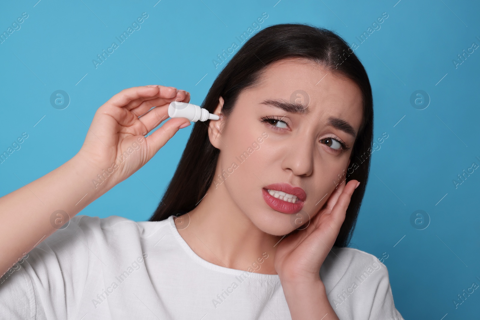 Photo of Young woman using ear drops on light blue background