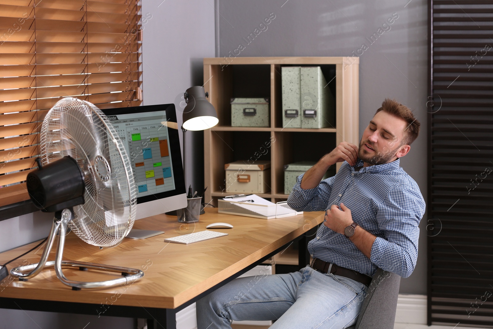 Photo of Man suffering from heat in front of fan at workplace