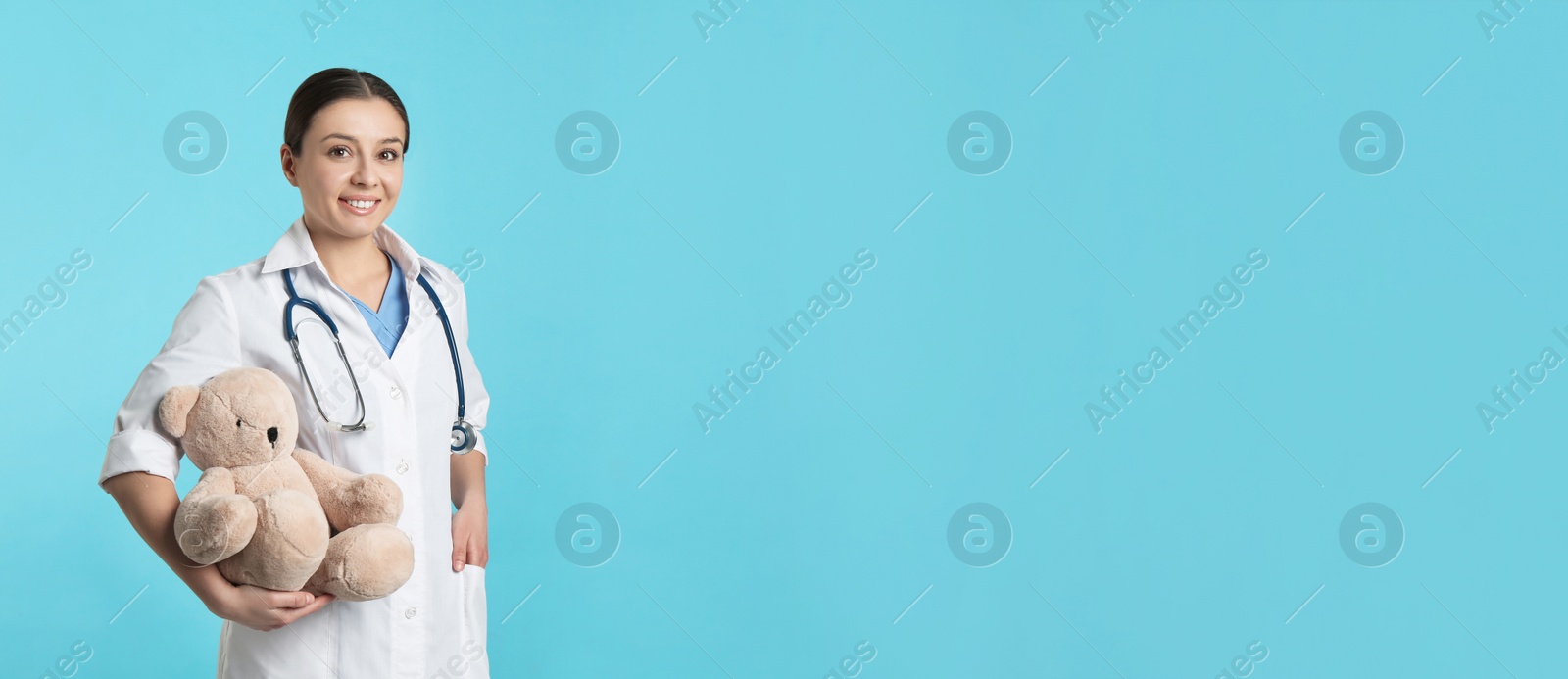 Photo of Pediatrician with teddy bear and stethoscope on turquoise background, space for text