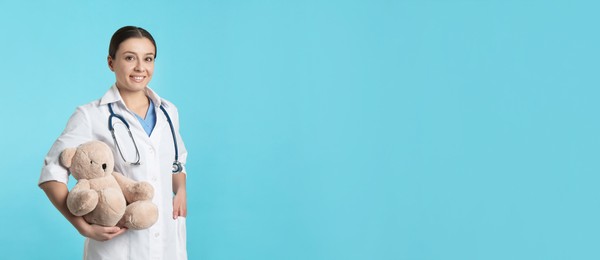 Photo of Pediatrician with teddy bear and stethoscope on turquoise background, space for text