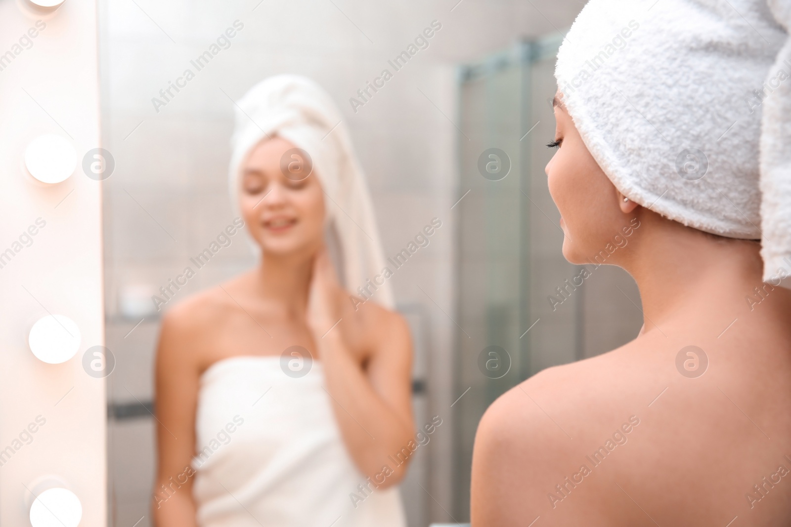 Photo of Beautiful woman with clean towels near mirror in bathroom