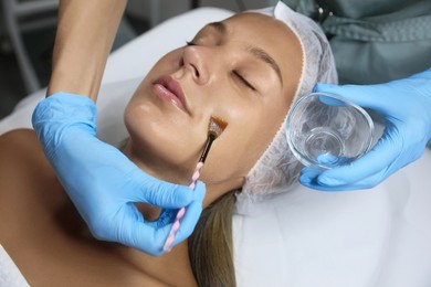 Photo of Cosmetologist applying chemical peel product on client's face in salon