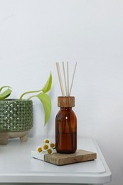 Aromatic reed air freshener, chamomiles and houseplant on white table