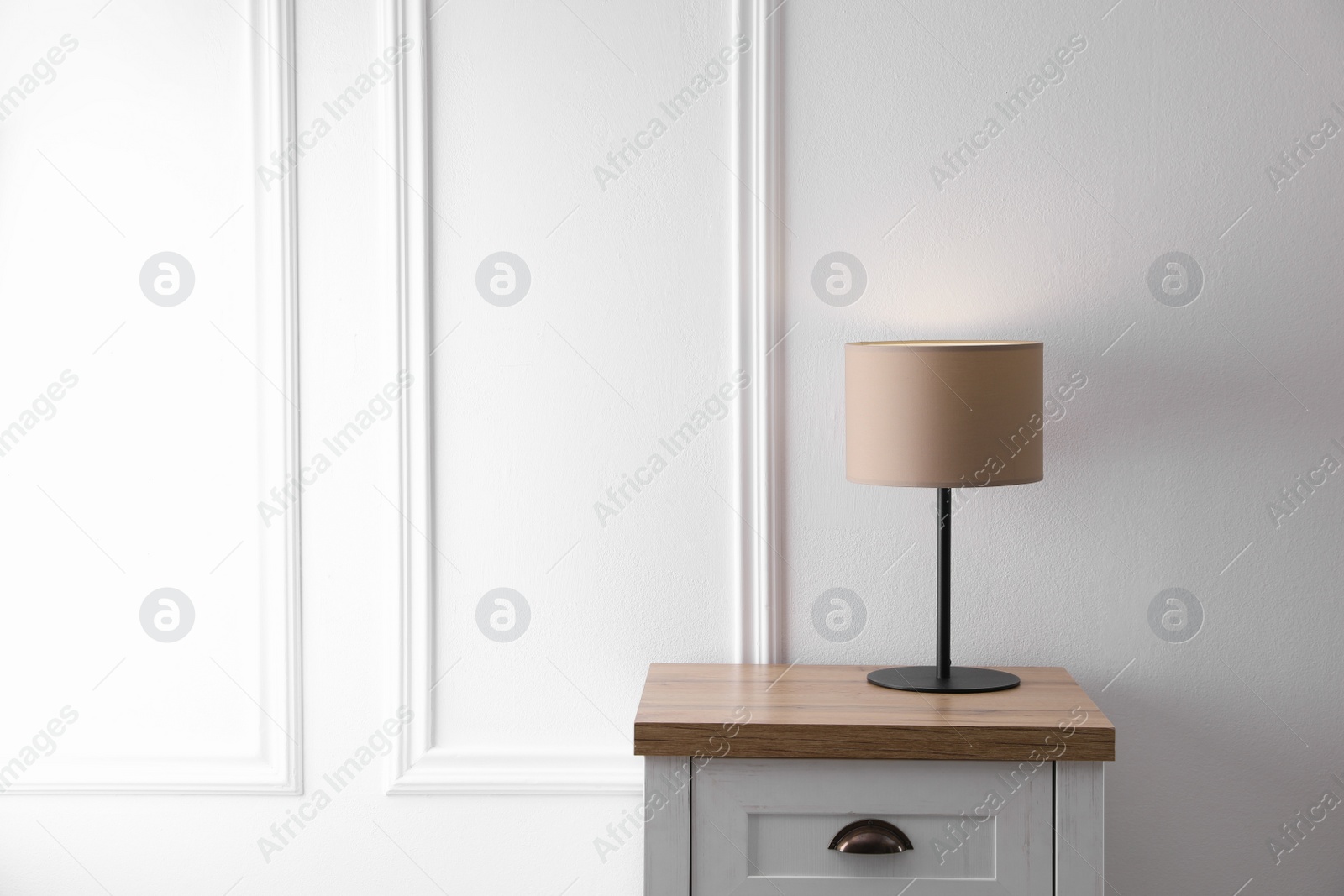 Photo of Wooden nightstand with lamp near white wall in room, space for text