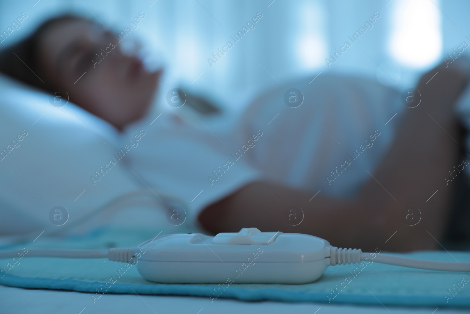 Photo of Young woman sleeping in bed with electric heating pad, focus on cable