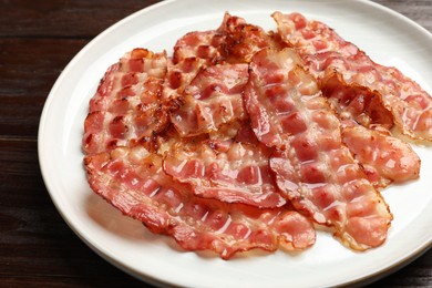 Photo of Plate with fried bacon slices on wooden table, closeup