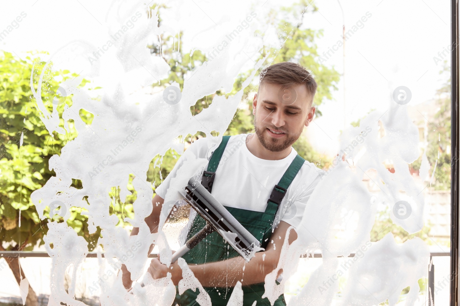 Photo of Male cleaner wiping window glass with squeegee from outside