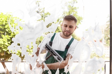 Male cleaner wiping window glass with squeegee from outside