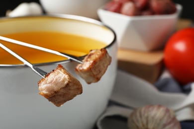 Fondue pot and forks with cooked meat on table, closeup