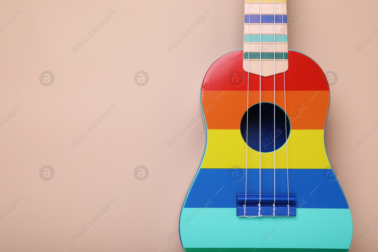 Photo of Colorful ukulele on beige background, top view and space for text. String musical instrument