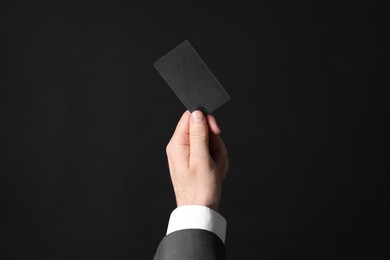 Photo of Businessman holding blank business card on black background, closeup