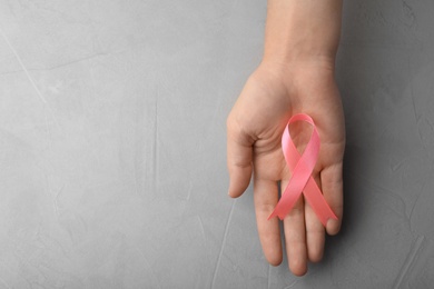 Woman holding pink ribbon on grey background, top view with space for text. Breast cancer awareness concept