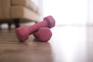 Pink dumbbells on floor in room, space for text. Home fitness