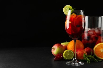 Photo of Glass and jug of Red Sangria with fruits on black table, space for text