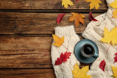 Cup of hot coffee, sweater and autumn leaves on wooden table, flat lay. Space for text